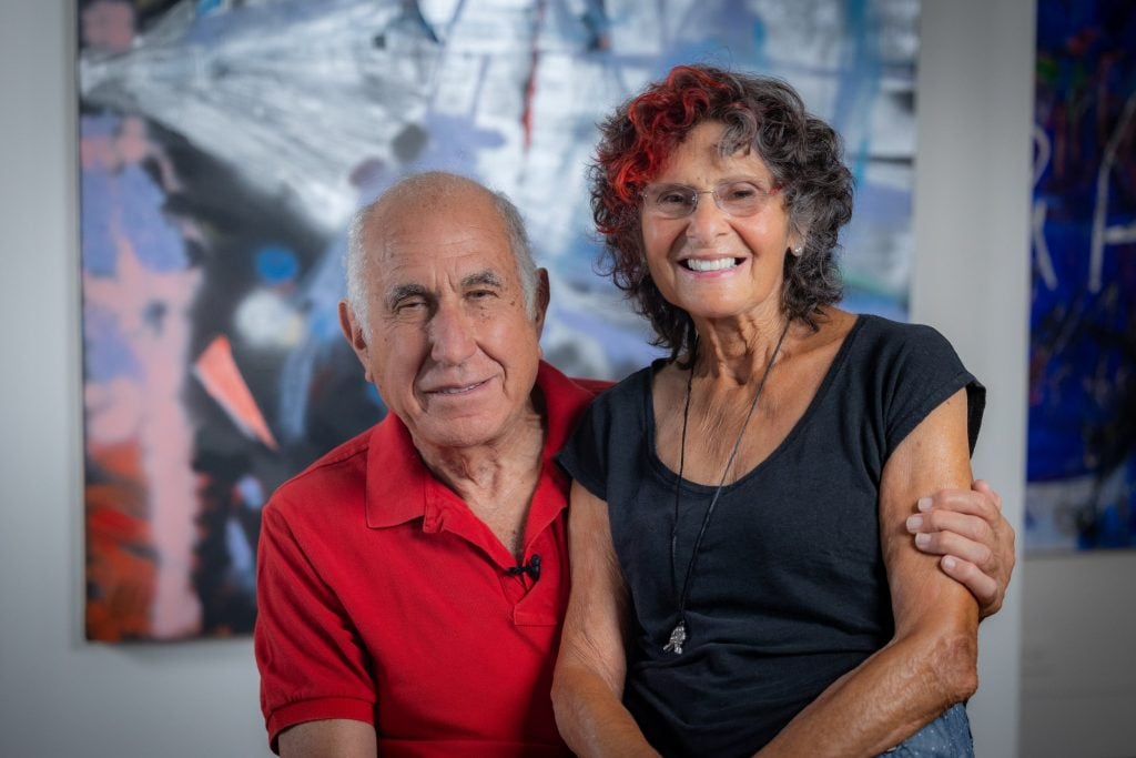 a man in a red polo shirt embraces a woman in a black blouse in front of a modern abstract painting