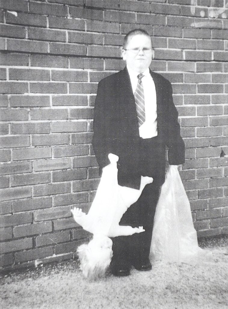 a black and white image of a young boy in a suit and tie holding a baby upside down