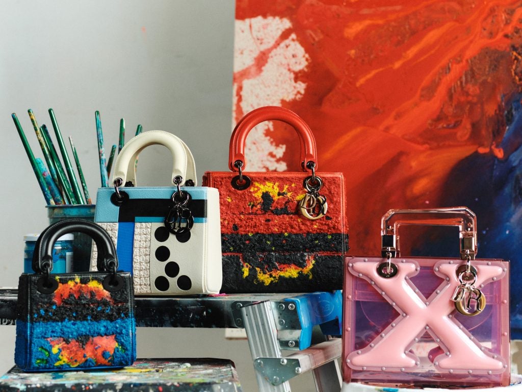 colorful purses are in front of a pot of brushes and an abstract painting 