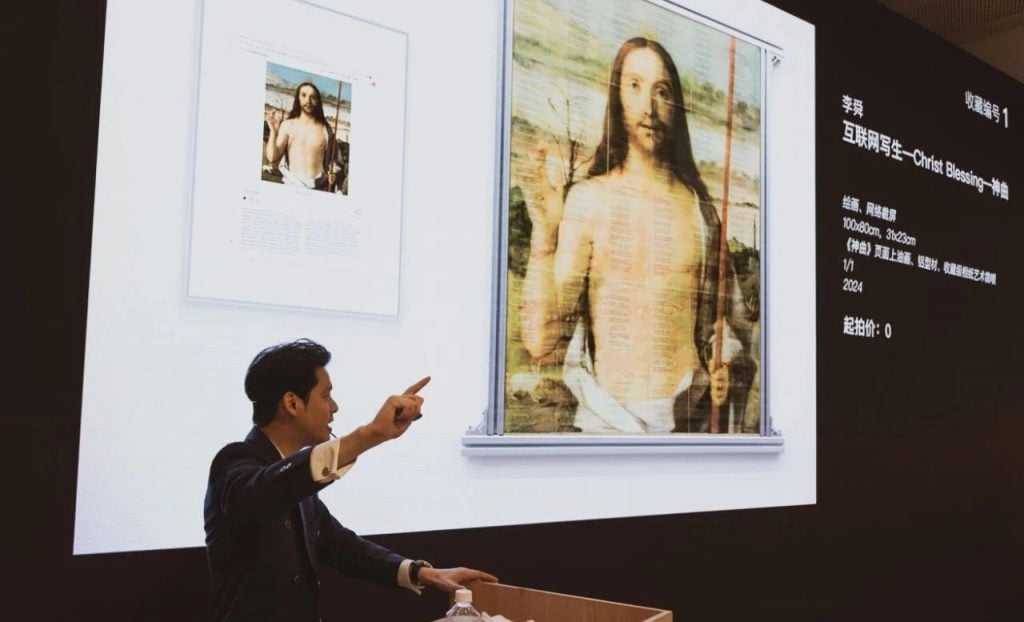 An auctioneer at a podium with a large screen behind him showing an artwork