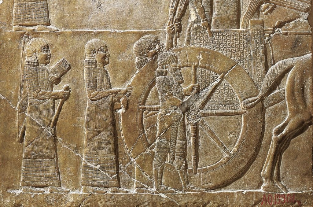 An ancient relief depicting a king riding high on a chariot surrounded by his servants