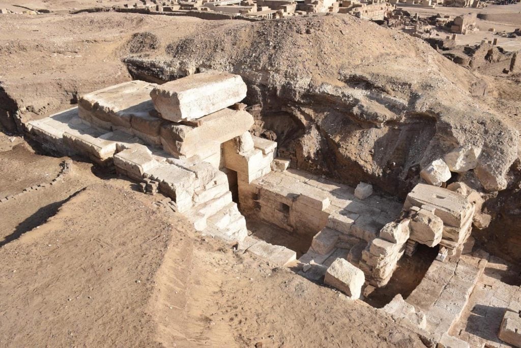 An ancient egyptian temple entrance is unearthed amongst beige rock.