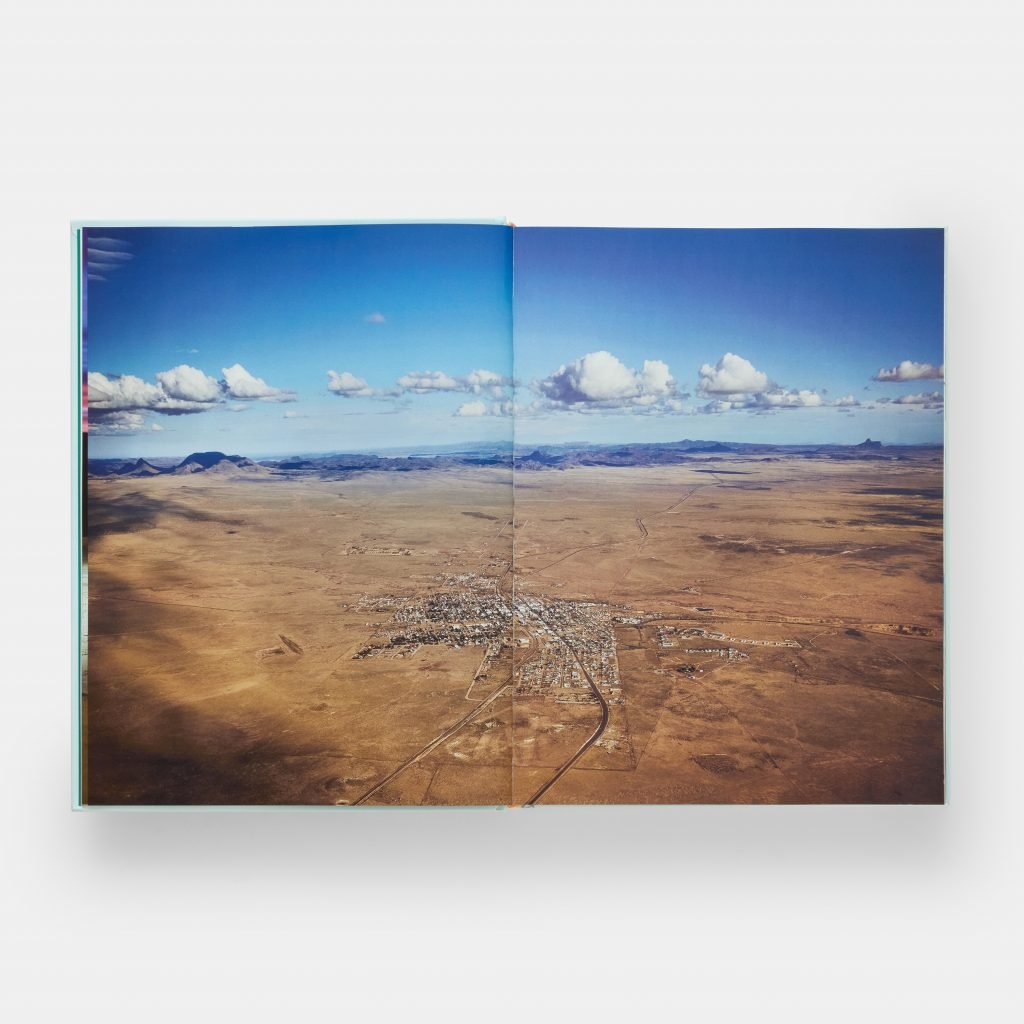 A photograph of a book opened to a full two-page spread featuring an aerial photo of Marfa, Texas.