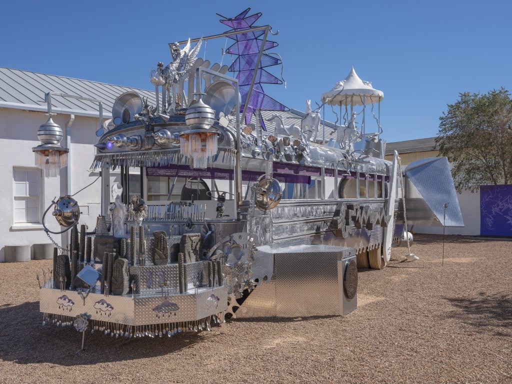 A photograph of a silver-painted, ornately adorned truck parked outside Ballroom Marfa beneath blue skies.