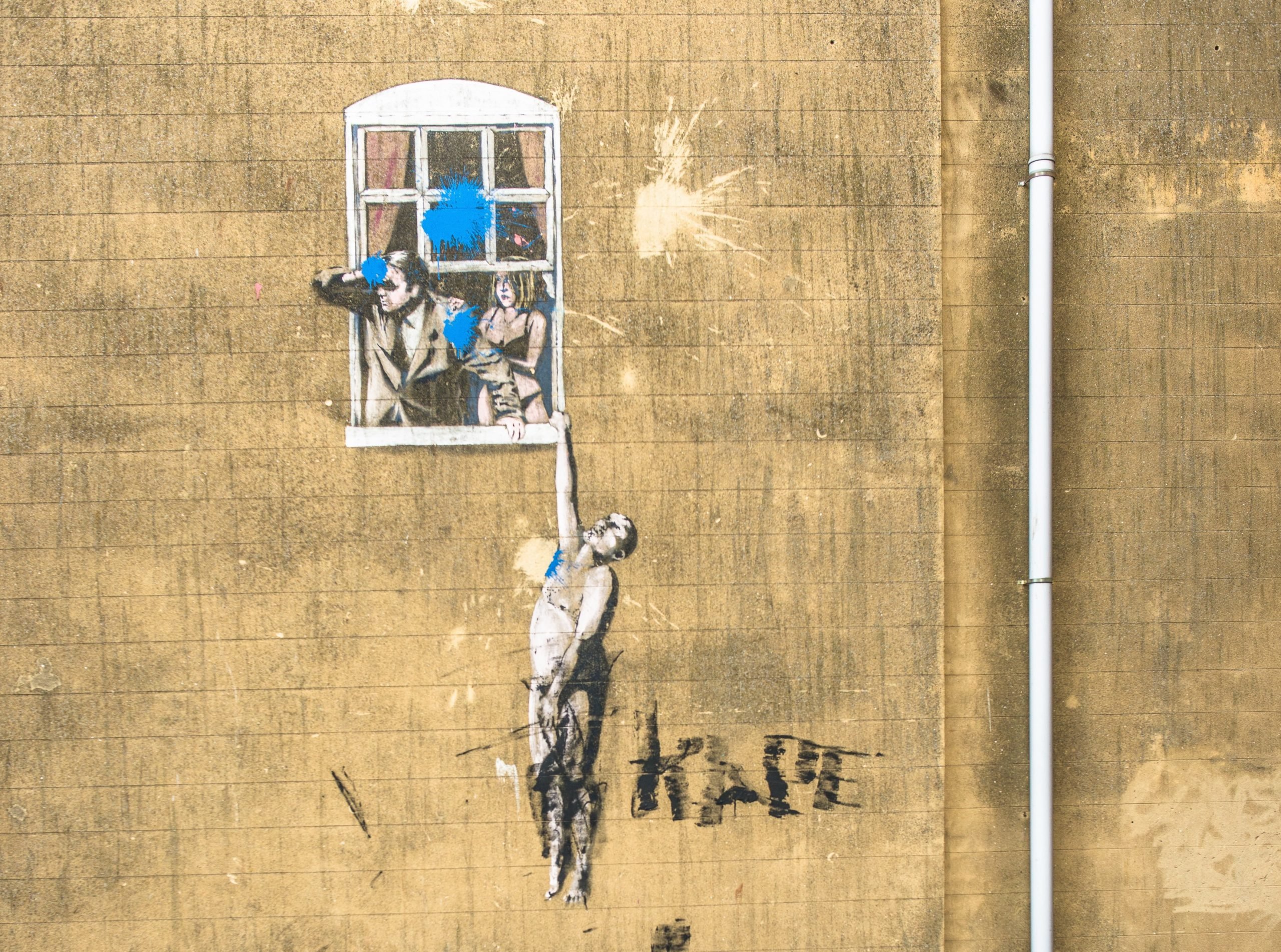 a street art stenciled painting of a man hanging from a window as two other people look out of the same window