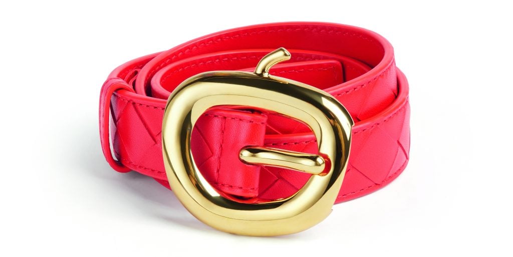 A photograph of a red leather belt rolled up with its apple-shaped gold buckle front and center.