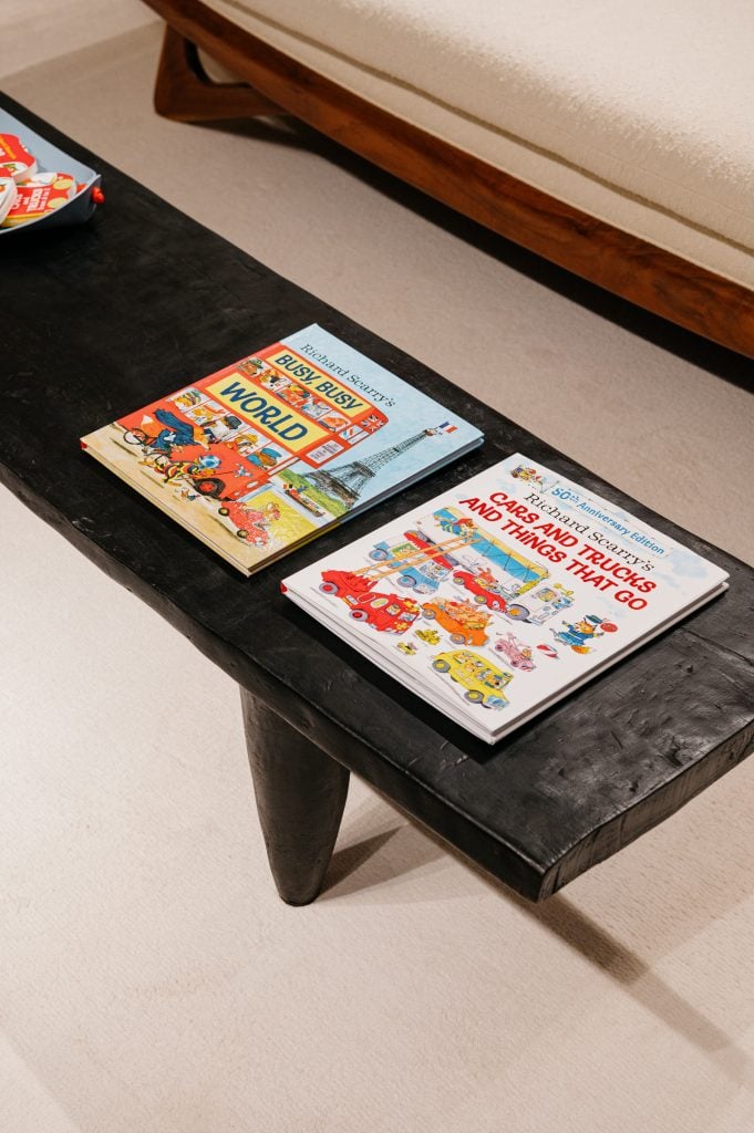 A photograph of three Richard Scarry books sitting on a black bench atop a white carpet in the new Bottega Veneta residence.