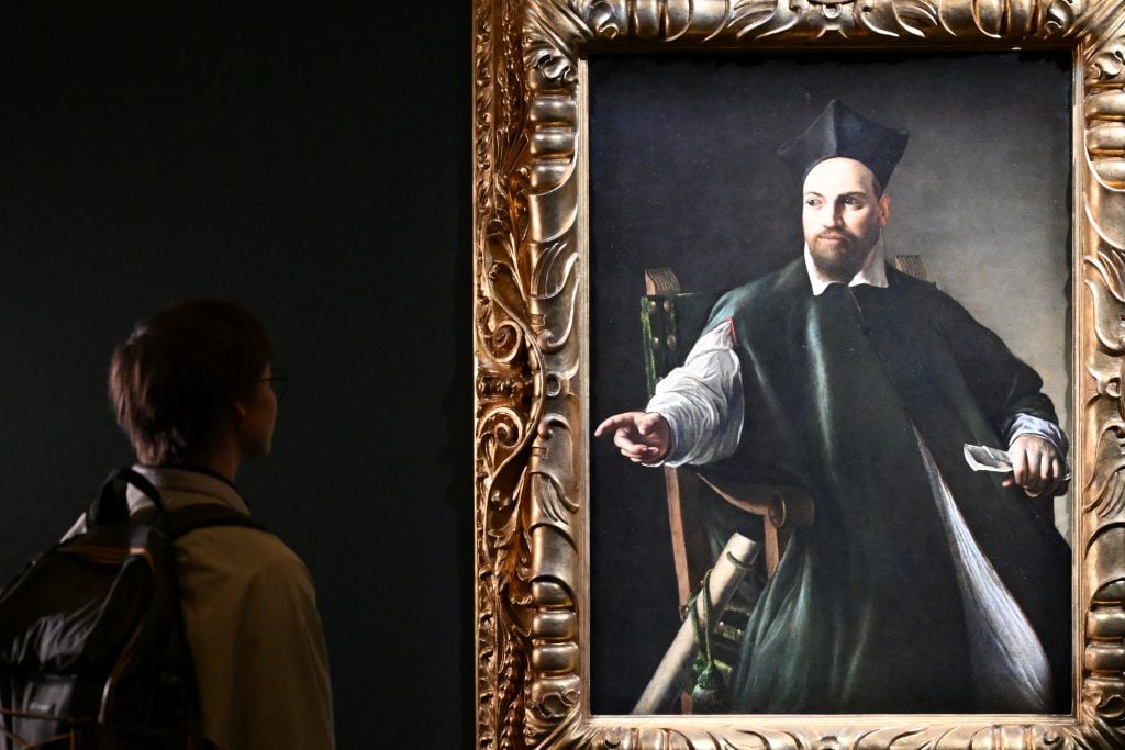 a boy standing in front of a painting of a man in a chair in a darkened room