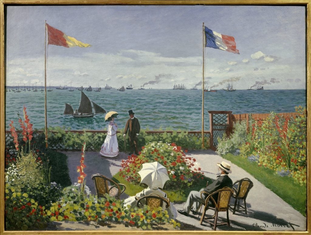 A painting depicting a vibrant garden with lush flowers, chairs, and umbrellas in the foreground. Two people, one holding a parasol, are seen walking and conversing near a railing that overlooks a vast blue sea. The sea is dotted with sailboats and steamships, and two flagpoles stand prominently, one displaying the French tricolor and the other a yellow and red flag