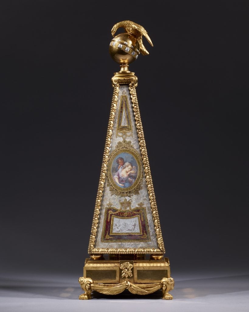 FAB Paris art fair highlight of a clock shaped like a tall pyramid with a golden eagle on a golden sphere at the top and intricate painting on its surfaces.