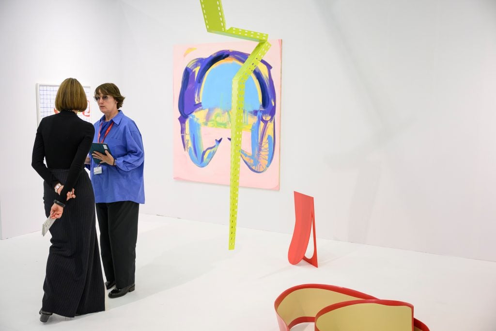 Two women standing in a white gallery with bright sculptures