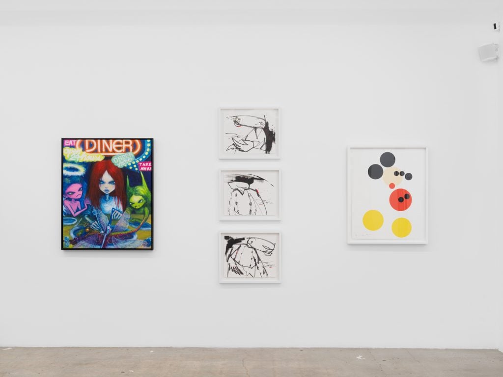 A white wall featuring a colorful painting, a column of three black and white artworks, and a geometric rendition of Mickey Mouse.