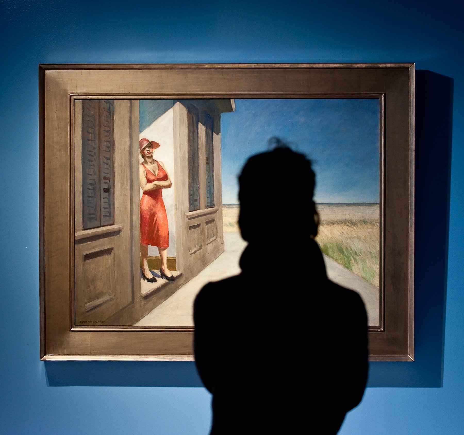 A visitor looks at a painting of a woman looking out from a building