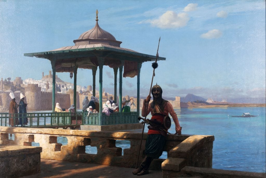 Painting by Jean-Léon Gérôme of a group of harem women in a pergola overlooking the sea in front of which is a stone rail on which an armed guard leans and looks back out at the viewer. 