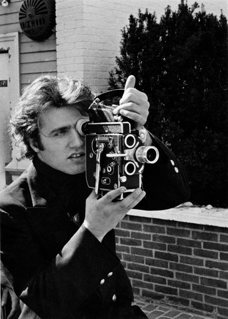 A man holding and looking into a film camera