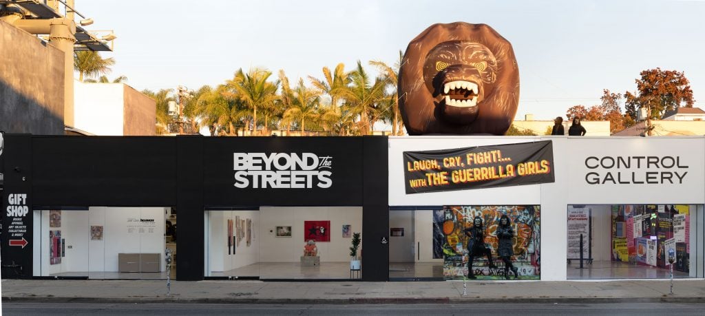 A photograph depicting the exterior of Beyond the Streets gallery, with an inflated Guerilla Girls gorilla head on top of it.