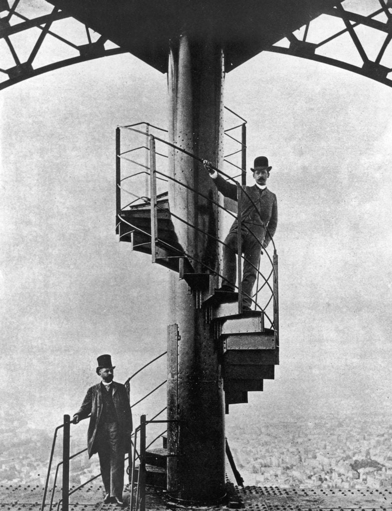 A man, Gustave Eiffel, posing on the staircase of the Eiffel Tower