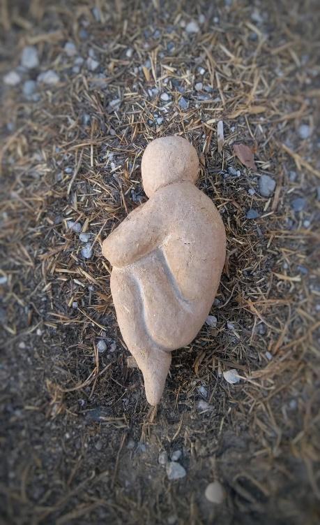 A small sculpture seemingly made from stone that shows a person in the fetal position