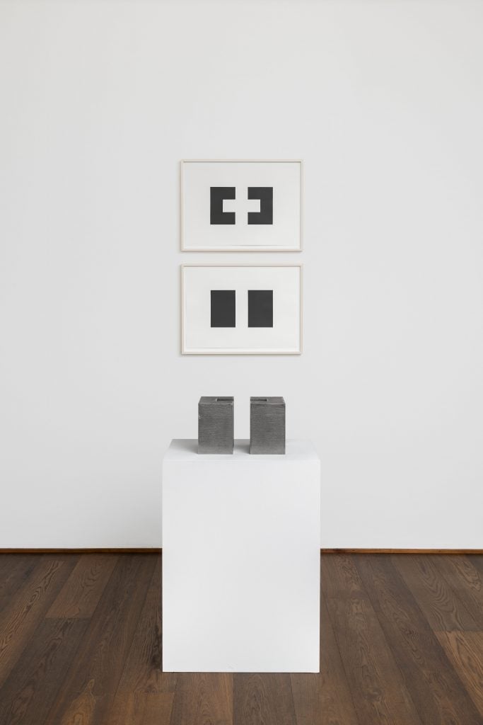 Installation view of "Frank Gerritz: Seraphic Light" showing a pair of minimalist prints above a rectangular minimalist sculpture on a pedestal.