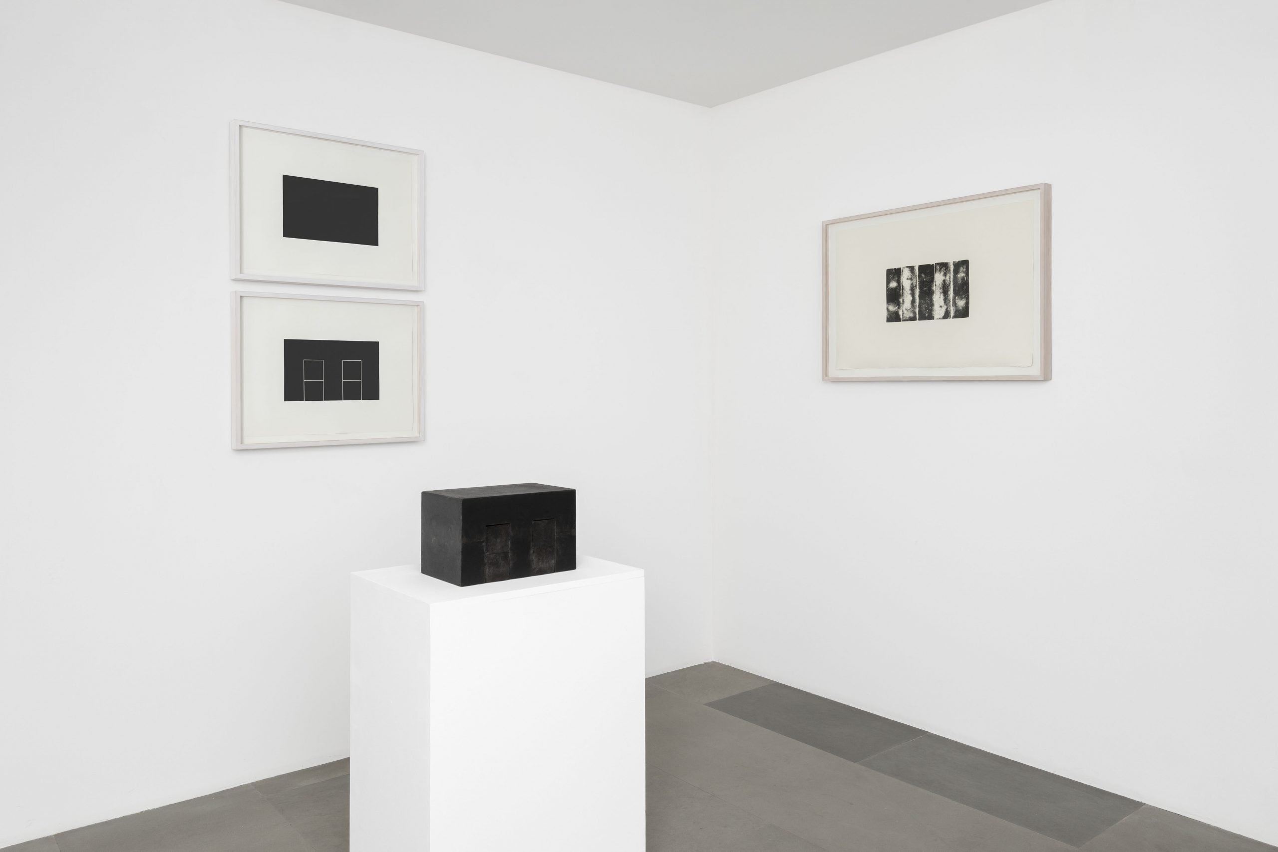 Installation view of "Frank Gerritz: Seraphic Light" showing a black rectangular sculpture on a plinth and two prints on the left wall and one on the right.