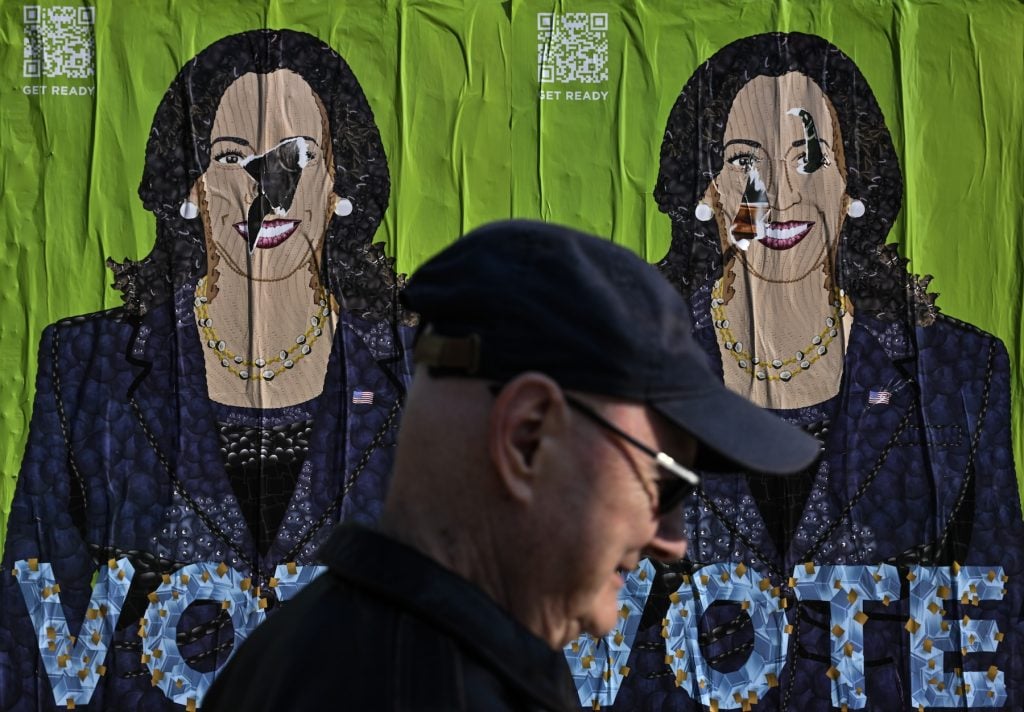 A man walks by two posters of a a woman's face that says VOTE