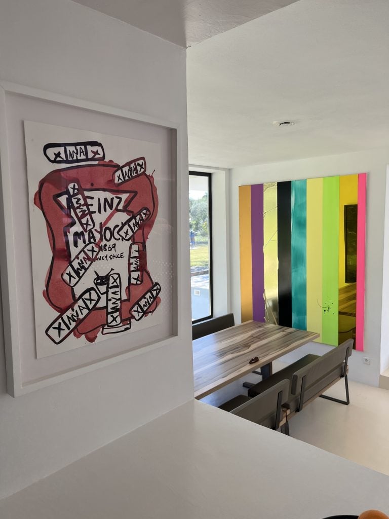 Two artworks installed in a dining space, on the left a print by Katherine Bernhardt and the right an abstraction in vertical colors by Ansem Reyle.