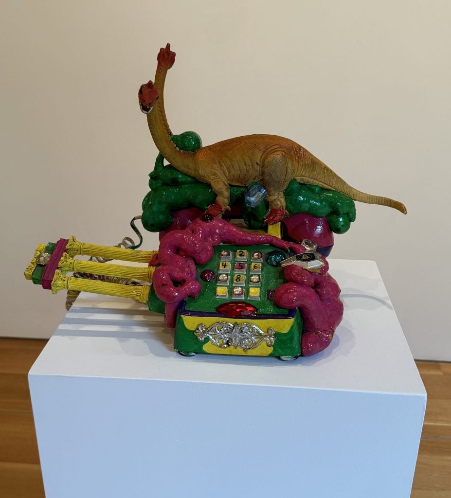 A photograph featuring a maximalist dinosaur-themed phone positioned atop a plain white plinth.