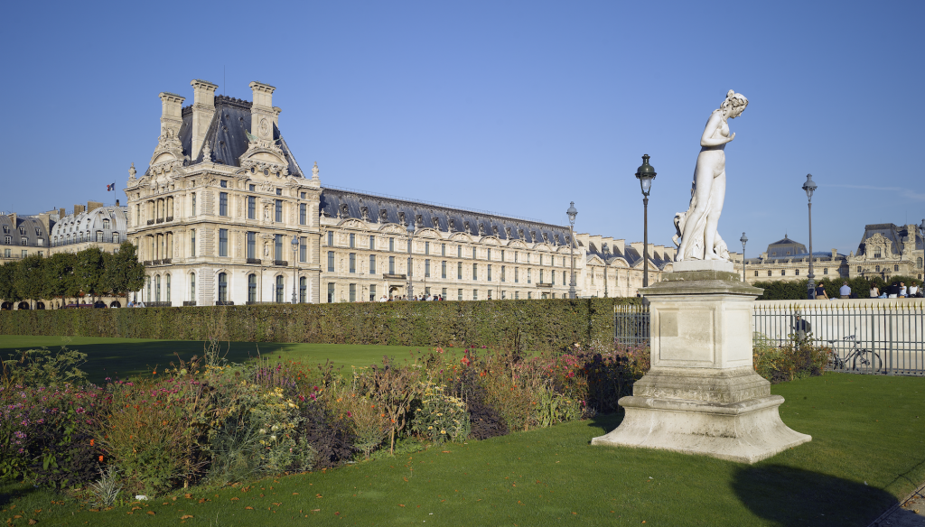 A photo of a palatial museum with a green lawn and a statue in front of it, all set beneath clear blue skies.