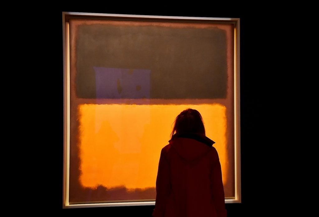 A woman silhouetted against an abstract brown and orange painting