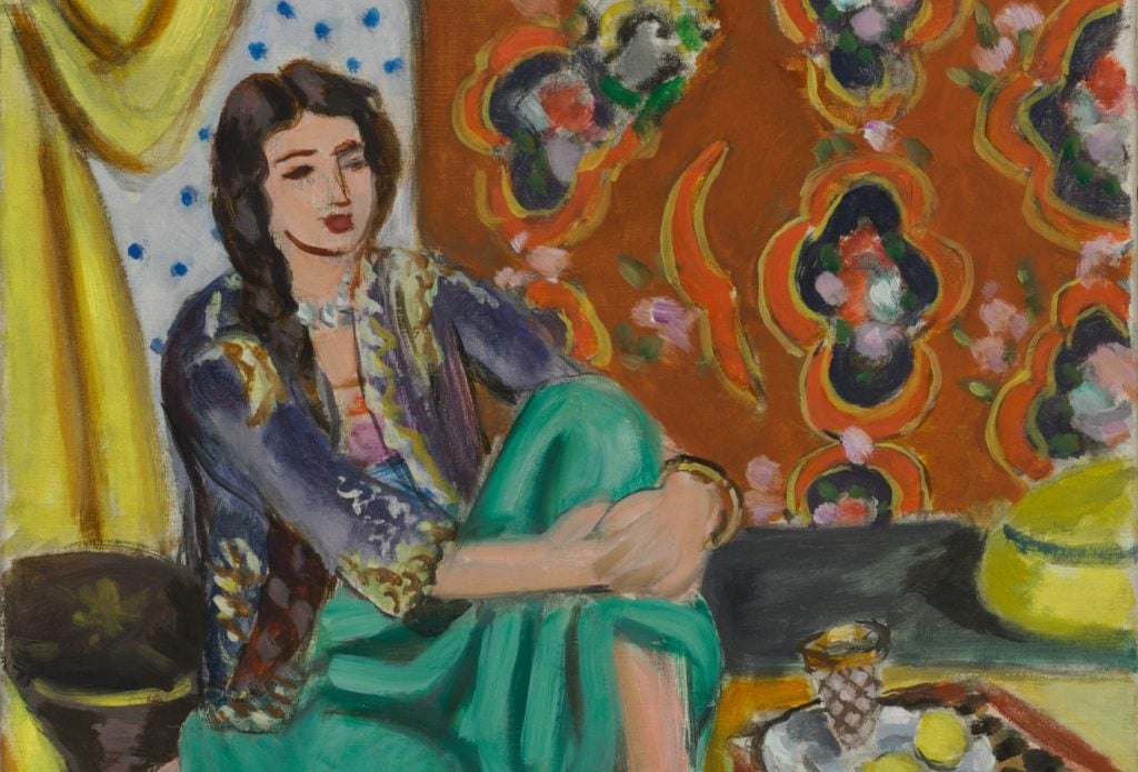 painting of a woman seated on a bench inside a home in front of richly patterned curtains wearing green sweatpants with her hands over her knees