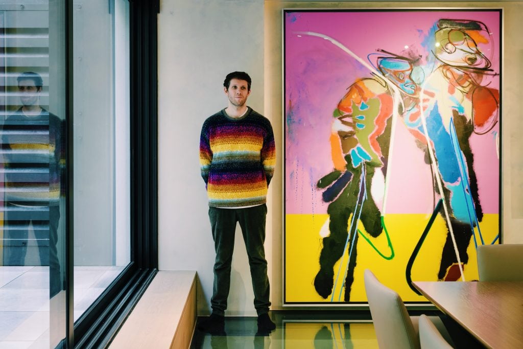 Dark Green founder Michael Doohan standing in a striped sweater next to a large-scale abstract painting by Daniel Richter.