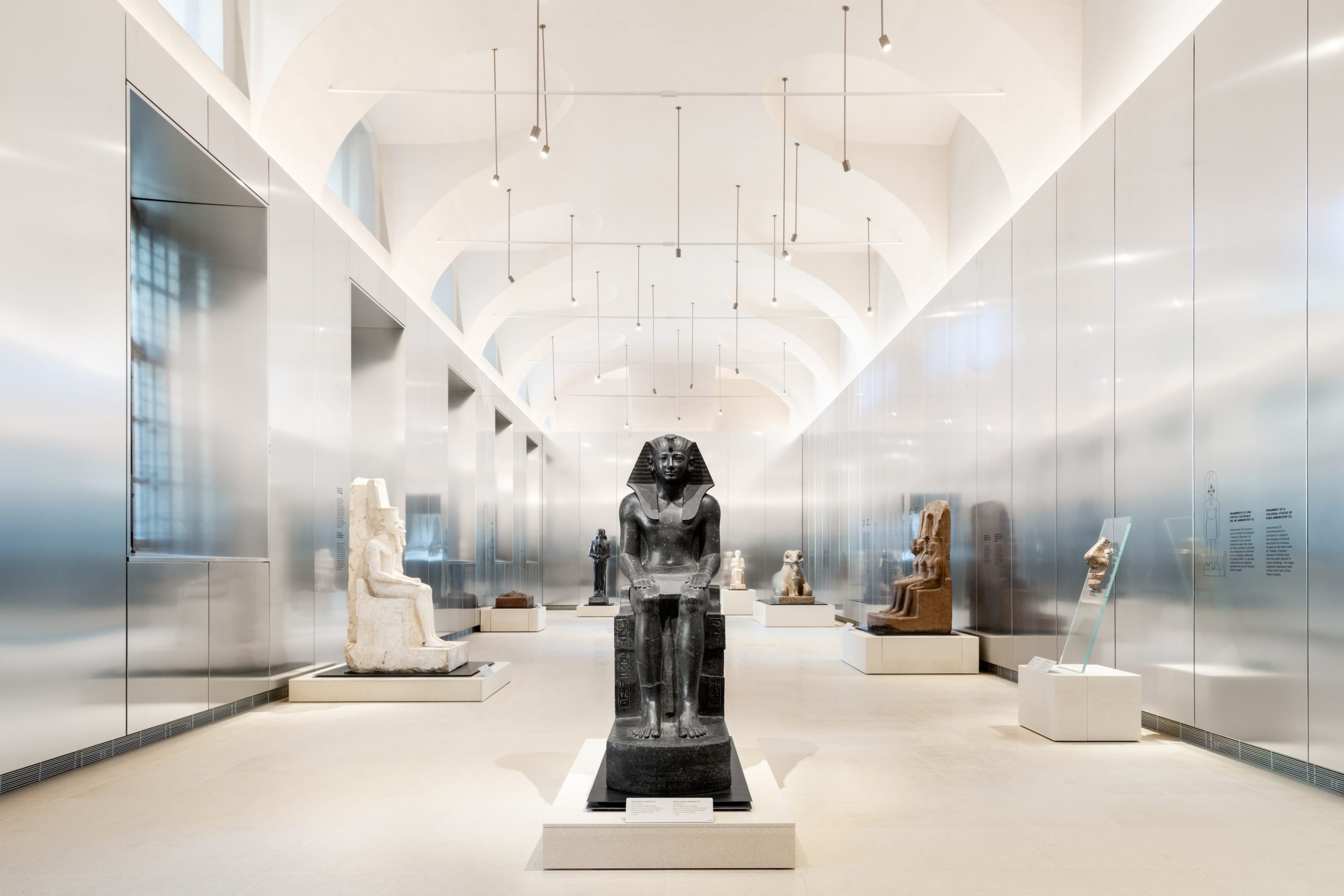 A silver metal-lined gallery space with ancient Egyptian statues in dark and white stone.