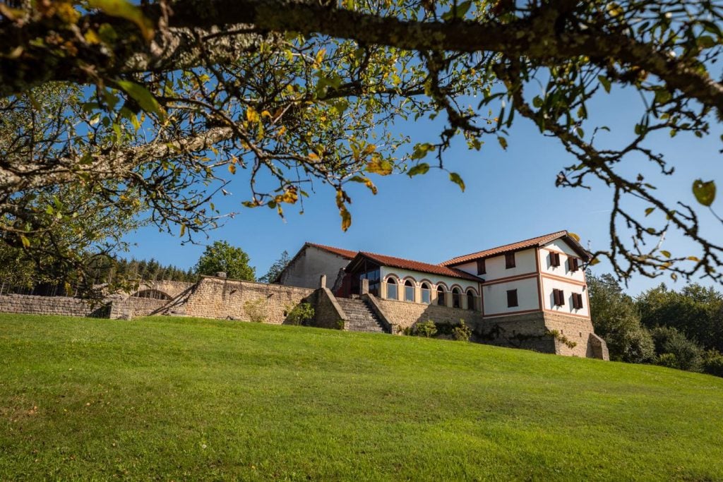 a roman villa shown atop a hill of green grass with blue sky in the background