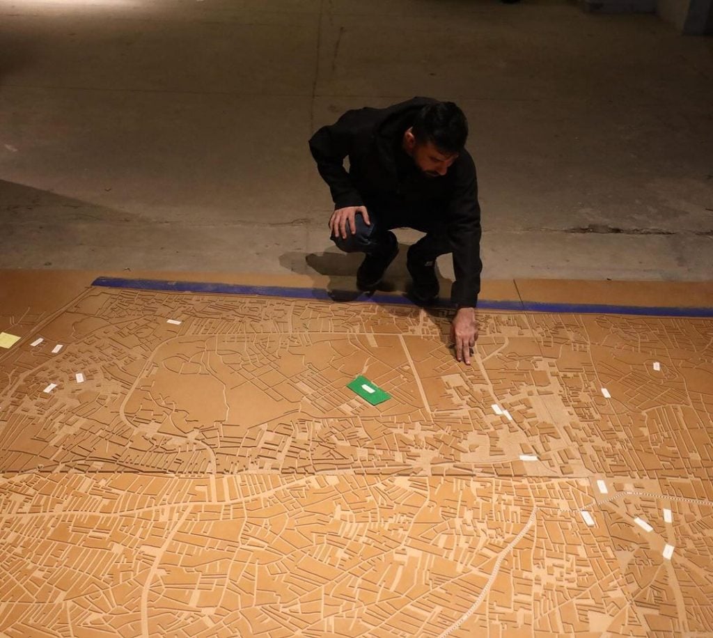 A person is seen interacting with a large wooden map of Gaza on the floor of an artist gallery space in Cairo