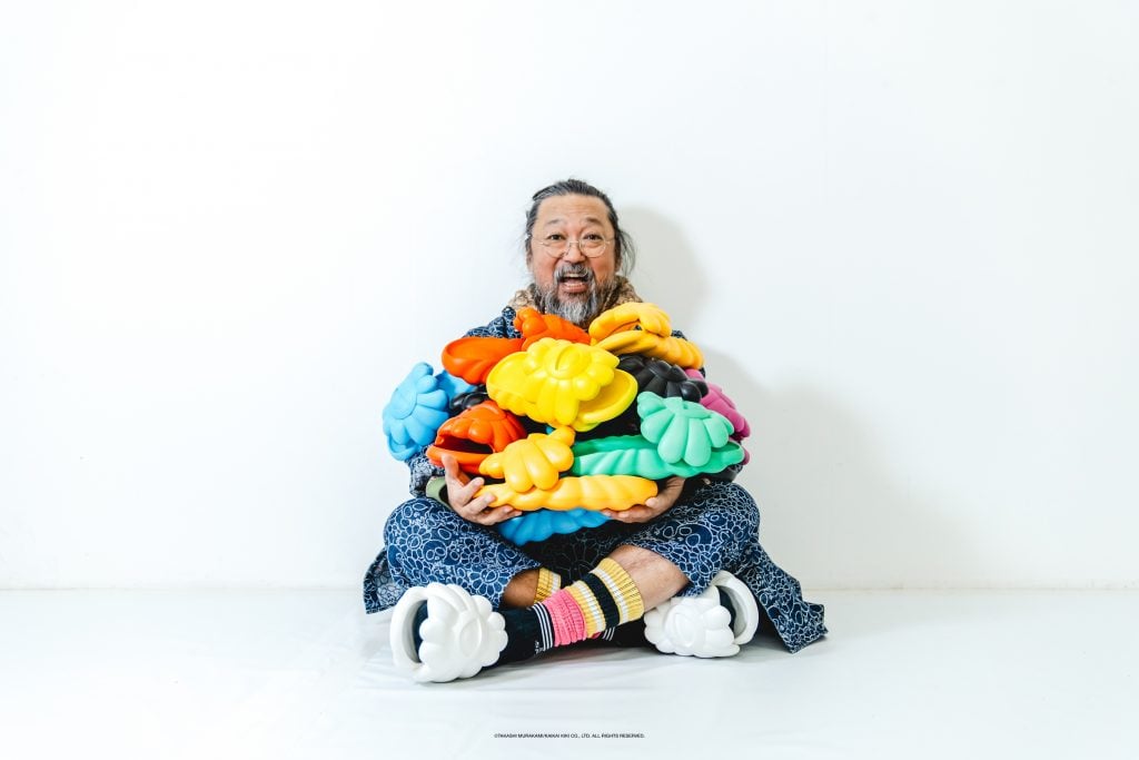 artist Takashi Murakami sits in a white room with an arful of multicolored shoes