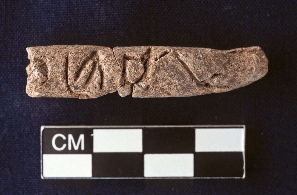 A clay cylinder featuring alphabet markings against a deep purple background