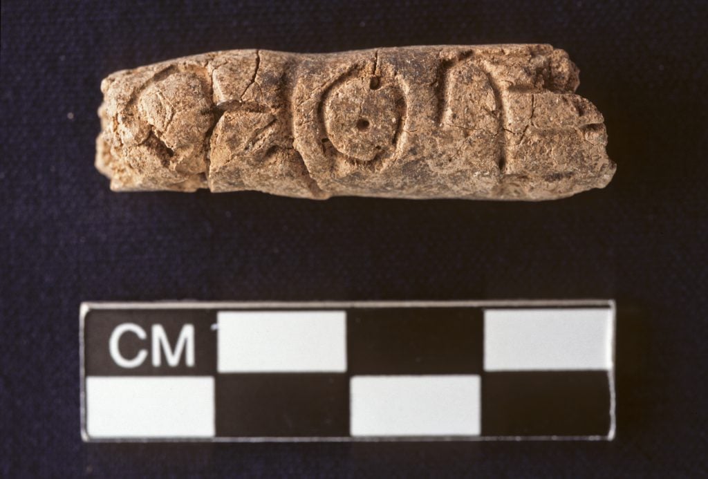 A clay cylinder featuring alphabet markings against a deep purple background