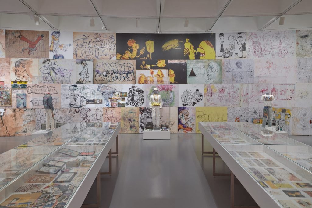 a large spacious room with two long rectangular tables covered in a huge amount of sketch paper depicting all kinds of drawings and designs inside a museum somewhere