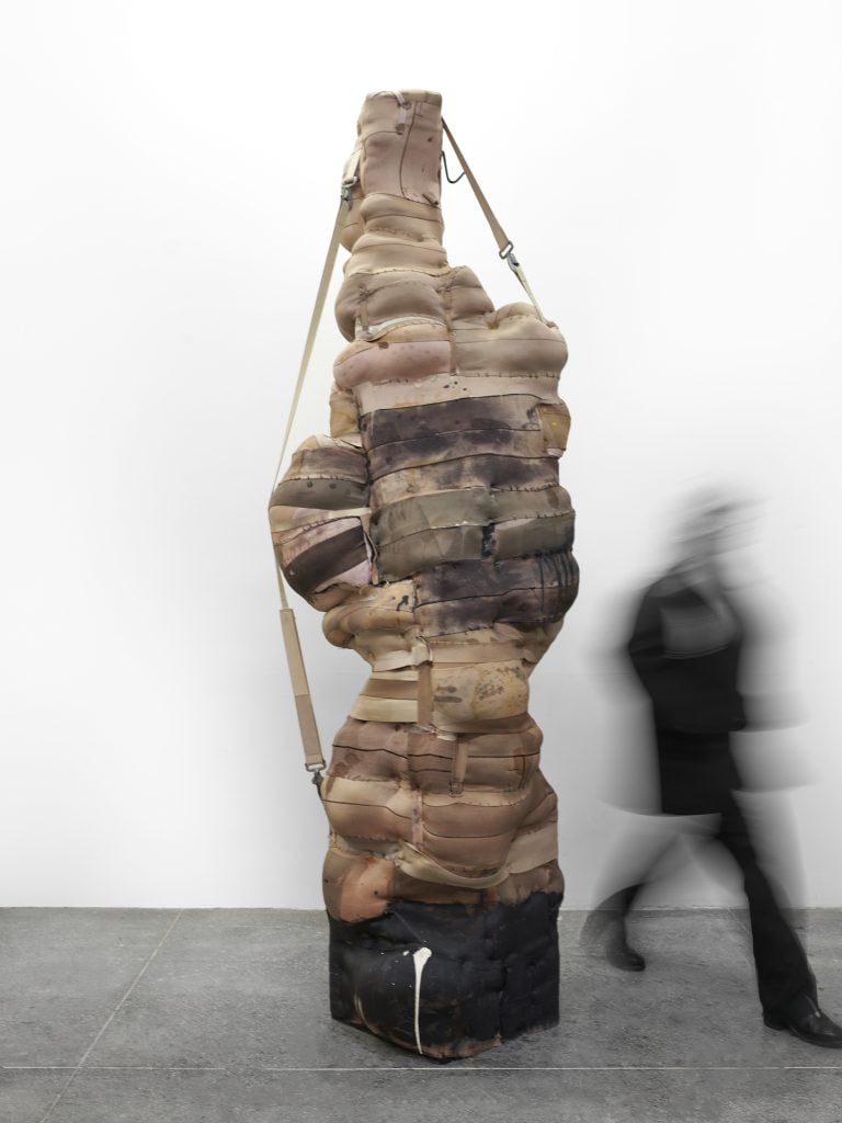 Sculptural assemblage by Patricia Ayres of an upright, more than six-foot-tall work made of stuffed dirty canvas fabric and ratchet strapped along its highpoint.