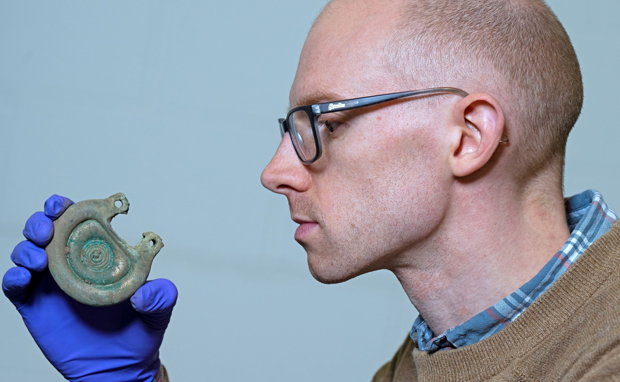 A man in glasses holding and looking at an ancient relic