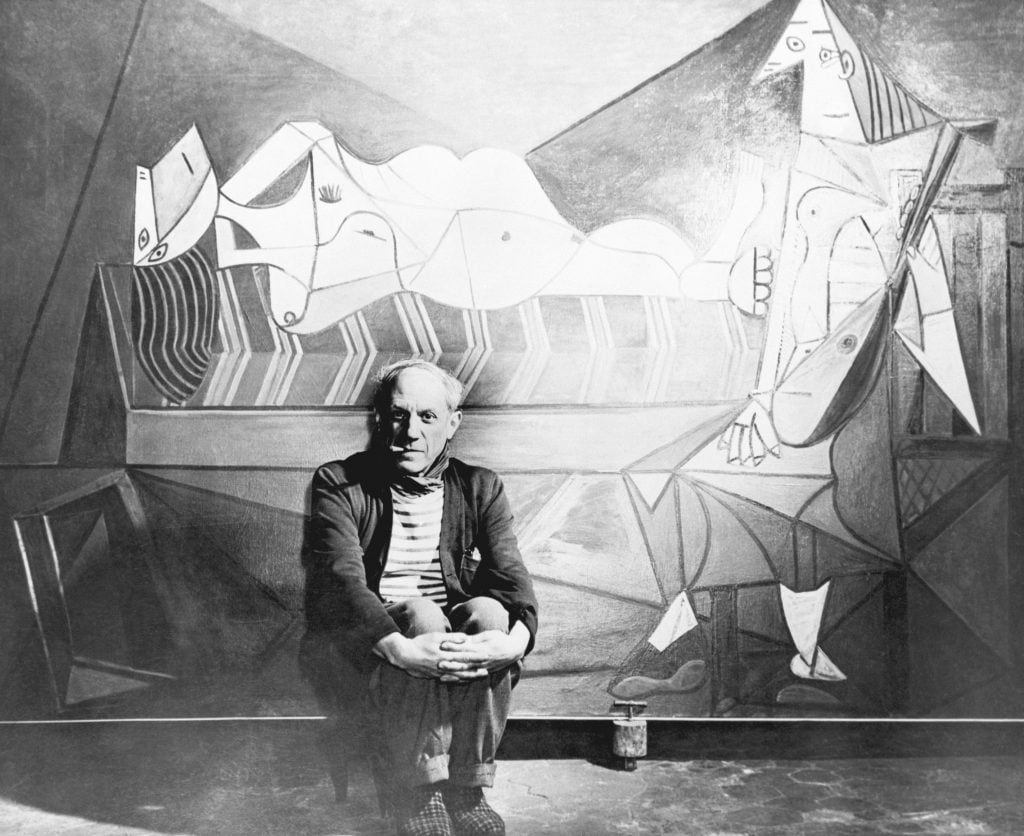 Pablo Picasso sitting in front of one of his paintings