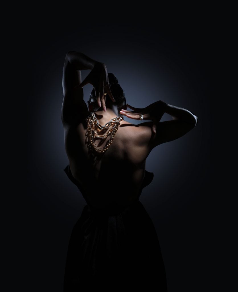 A dark, dramatic photograph featuring the strong back of a figure draped in Pomellato jewels.