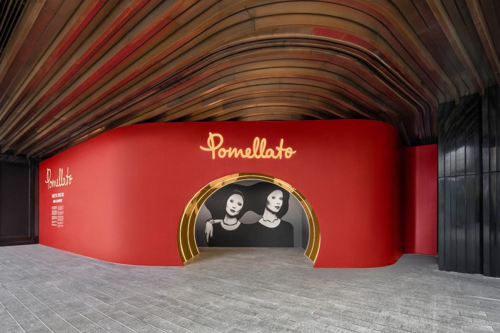 A photograph of the red entryway to the Pomellato retrospective, with a black and white photograph visible through its circular portal.