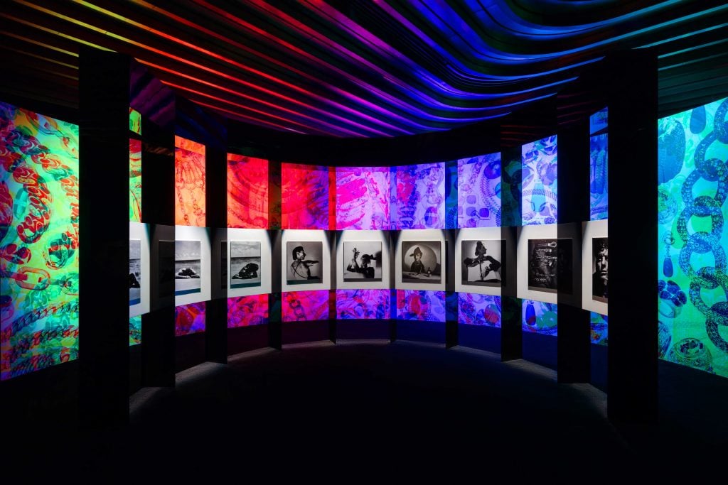 A photograph of a dark room ringed with rainbow-colored panels each holding a different black and white photo from a 1980s Pomellato ad.