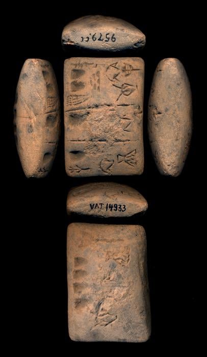 A photograph of a light brown prehistoric tablet emblazoned with cuneiform, on a black background.