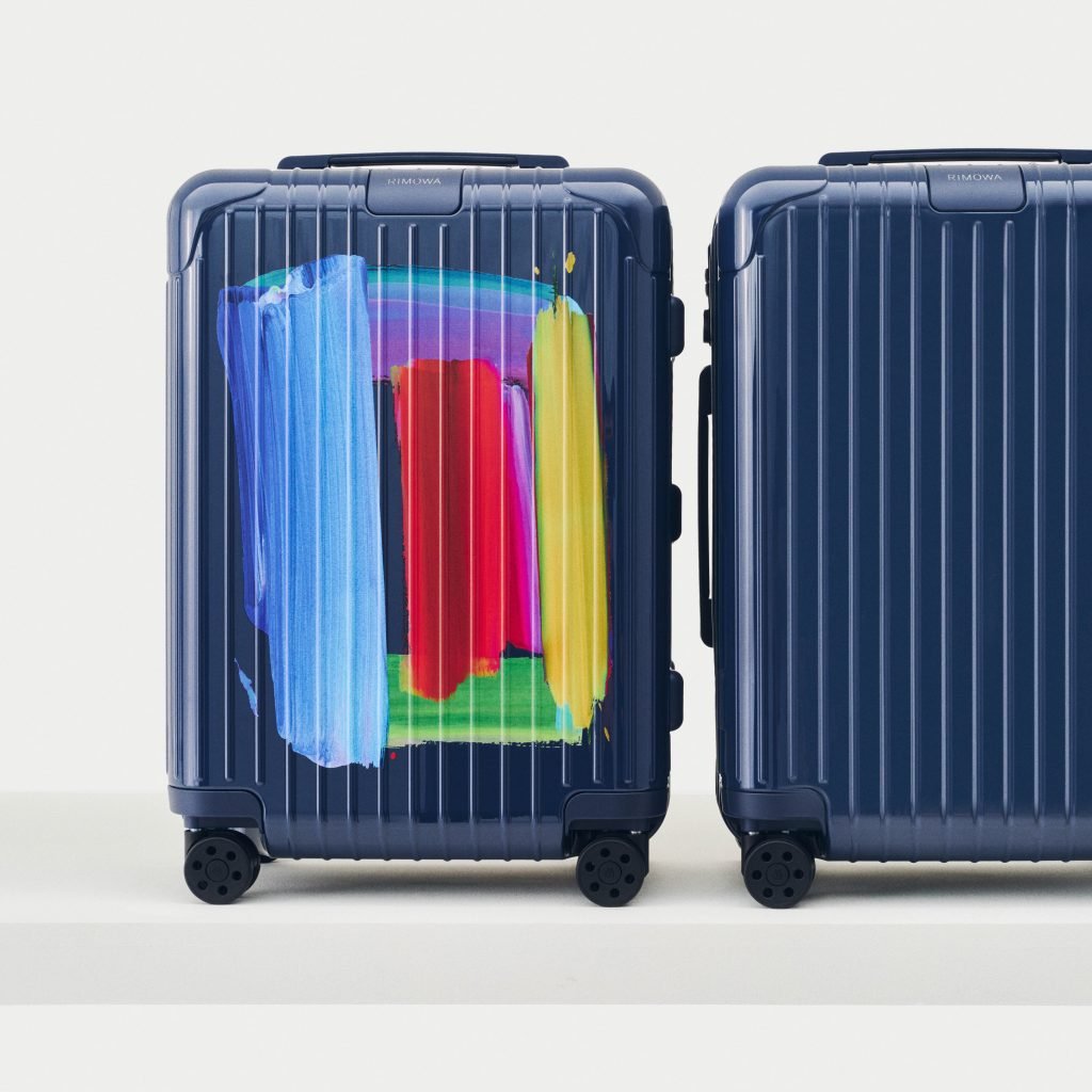 A photograph of two deep blue suitcases standing side by side—the one on the left faces forward and displays a brightly colored abstract artwork, while the one on the right show's the suitcase's plain blue backside.