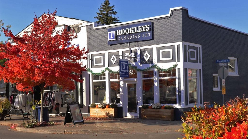 Exterior view of Rookleys Canadian Art in Ridgeway, a grey and white storefront with a maple out front that has turned red.