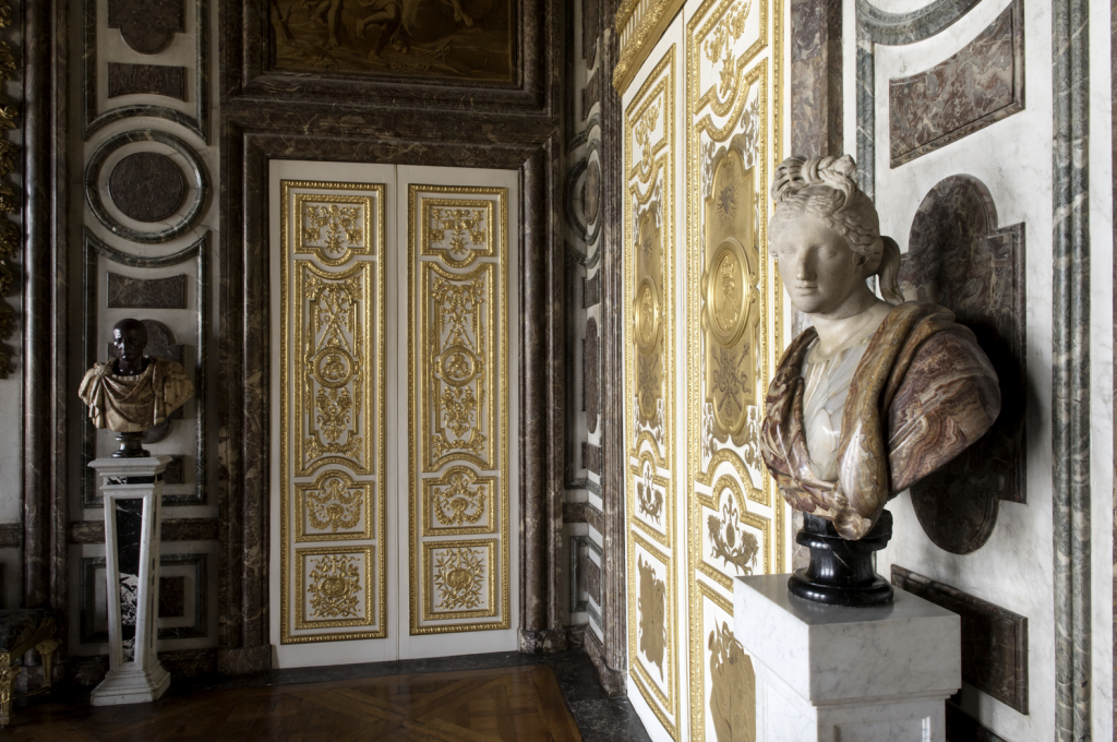 A photograph of marble busts punctuating the gold-painted and marble walls of Le Salon de Diane in Vesailles.