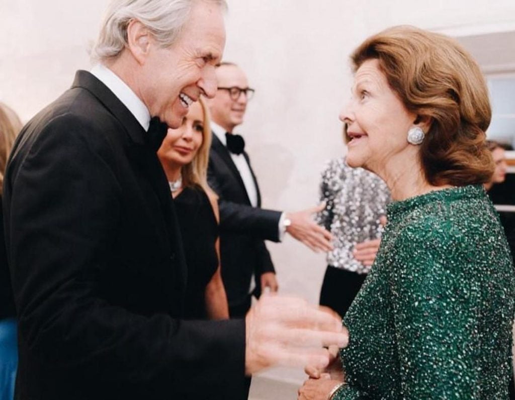 A man in a tuxedo greets a glamorous woman in a green sparkly dress