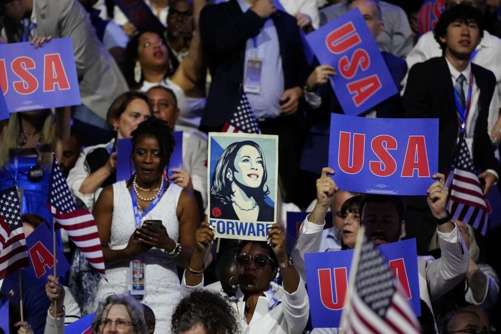 An image of a crowd with someone holding up a poster of a woman that says FORWARD at its center